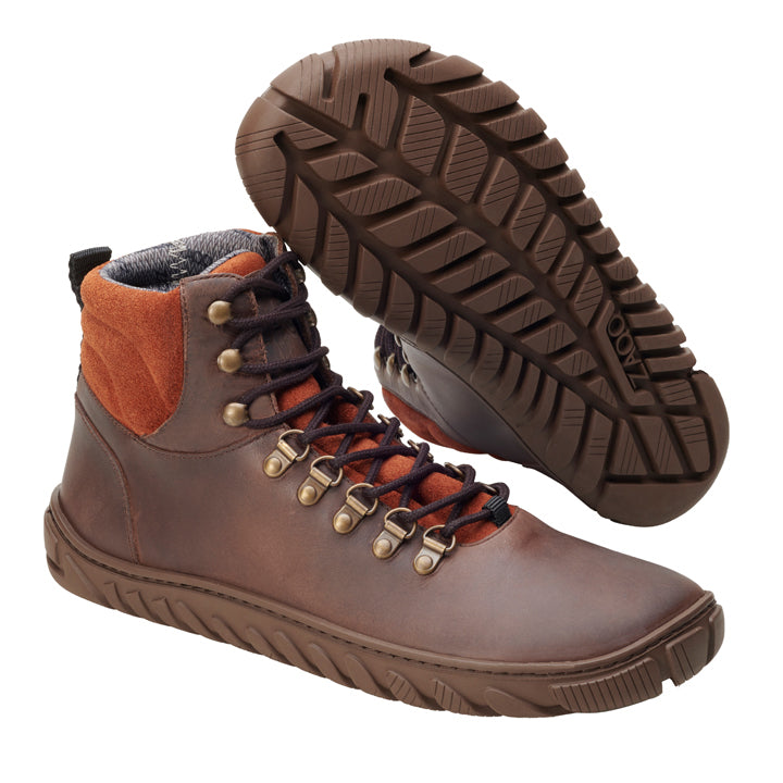 Wir präsentieren die ZAQQ WALQ Brown Waterproof-Stiefel: ein Paar High-Top-Lederschuhe mit auffälligen roten Veloursleder-Akzenten und kontrastierenden schwarzen Schnürsenkeln. Diese vielseitigen Winterschuhe sind mit einer strapazierfähigen, strukturierten Sohle ausgestattet, die sich perfekt für Outdoor-Abenteuer eignet. Ein Stiefel wird aufrecht präsentiert, während der andere angewinkelt ist, um seine robuste Sohle hervorzuheben.