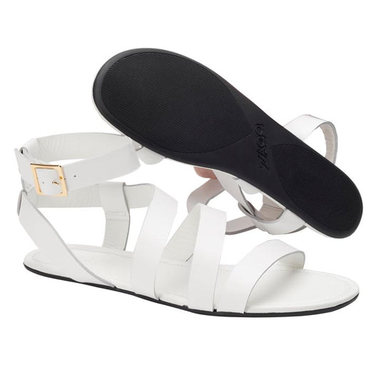 Die MONIQ White Gladiator-Sandalen von ZAQQ bestechen durch ihr schickes Design mit mehreren Riemen und einer goldenen Schnalle. Eine der Sandalen steht aufrecht, während die andere abgewinkelt ist, sodass die schwarze Sohle mit ZAQQ-Branding sichtbar ist. So werden Stil und Komfort mühelos miteinander kombiniert, ähnlich einer Barfußsandale.