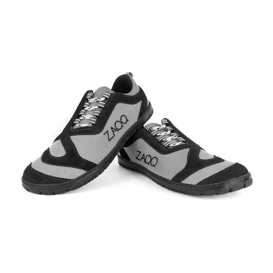 Ein Paar QUIQ Trail Black Vegan-Sportschuhe von ZAQQ in schwarz-grauem Design mit atmungsaktivem Netzgewebe zur Belüftung und dicken Gummisohlen zur Unterstützung. Sie sind so positioniert, dass ein Schuh auf der Sohle des anderen ruht.