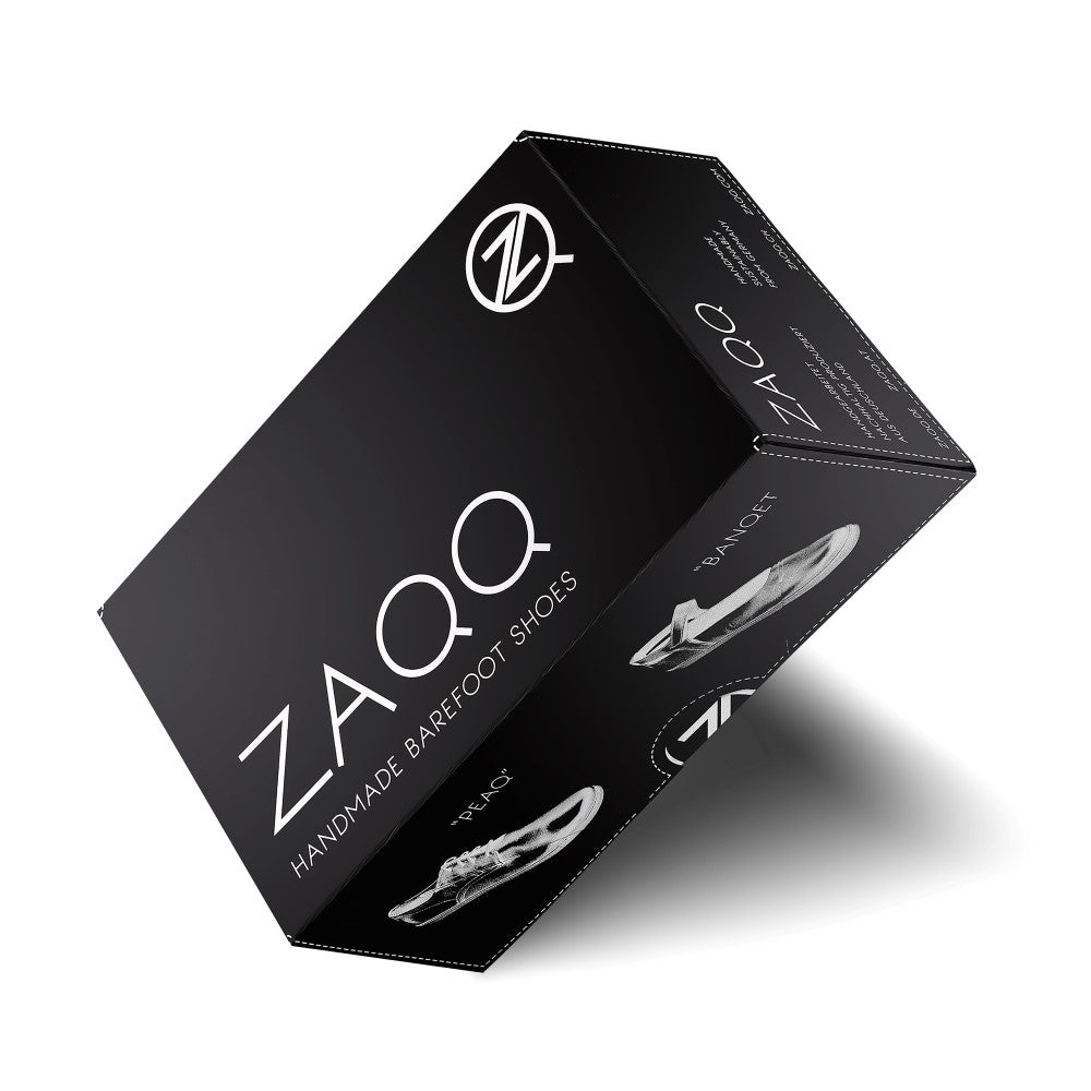 Eine schwarze Box mit dem Aufdruck „SPARQ Low Black White“ von ZAQQ, einem Logo und dem Bild eines eleganten Barfußschuhs. Die Box, die an luxuriöse Sneaker aus Nappaleder erinnert, steht schräg vor einem makellos weißen Hintergrund.