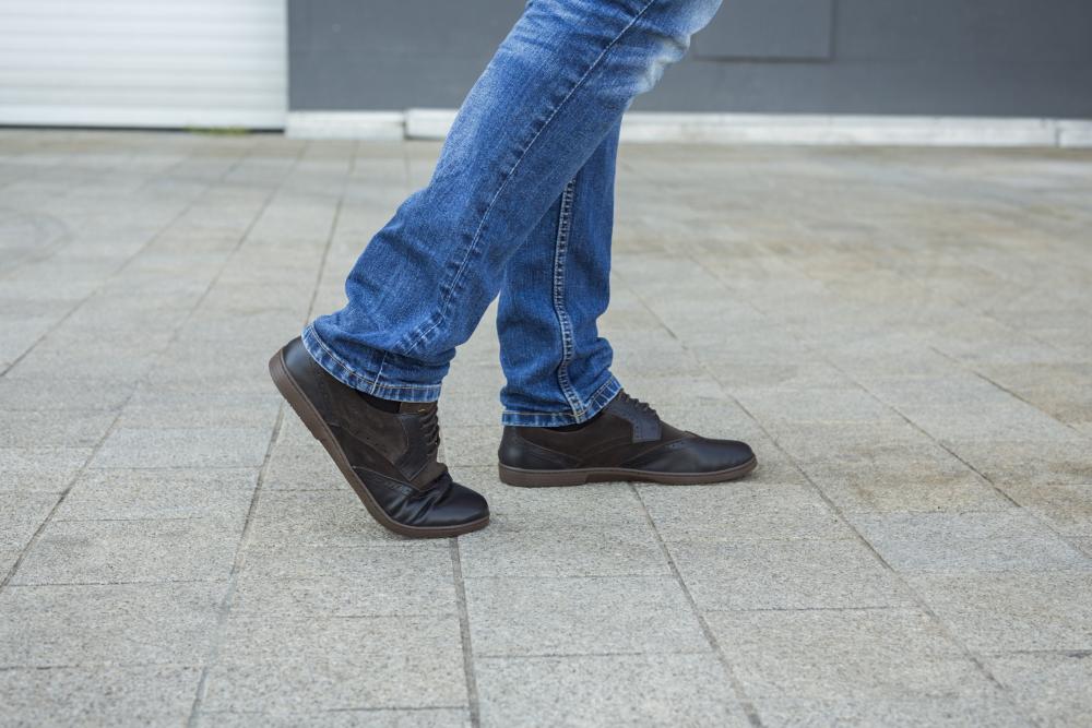 Eine Person in Blue Jeans und schwarzen BRIQ Brogue Tonka Businessschuhen von ZAQQ läuft auf einem gefliesten Boden. Das Bild fängt die untere Körperhälfte ein und betont die Bewegung beim Gehen.