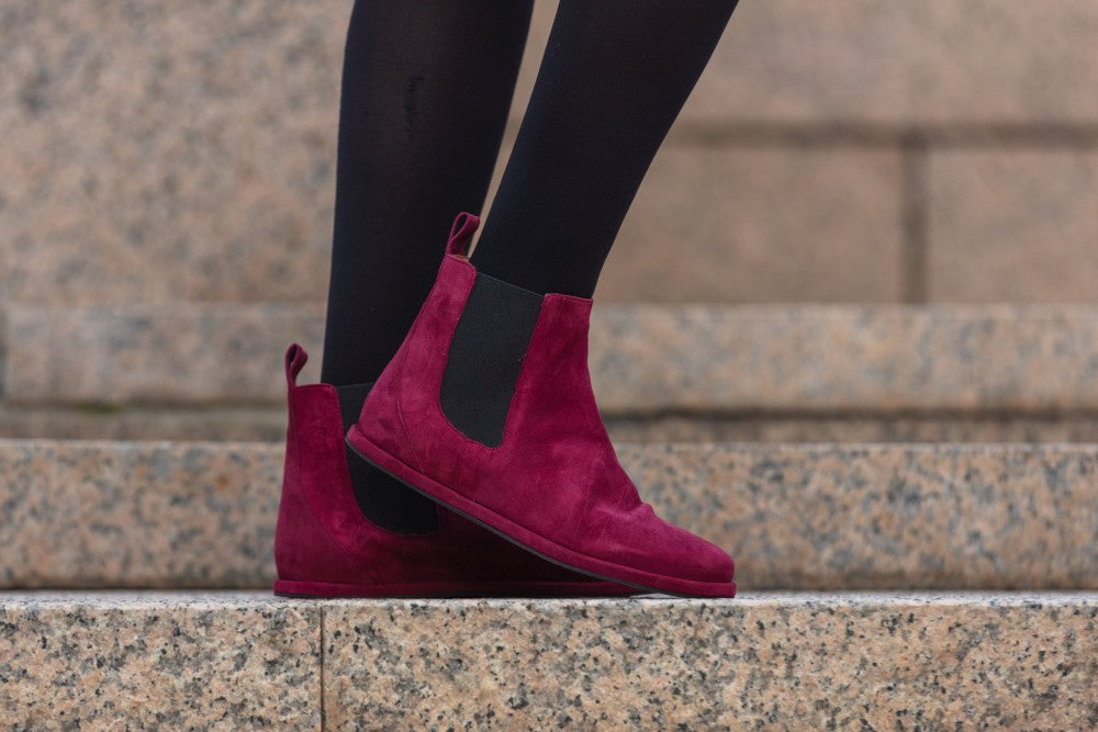 Eine Person steht auf Steinstufen und trägt schwarze Leggings und leuchtend rote ZAQQ EQUITY Berry Chelsea Boots aus Wildleder.