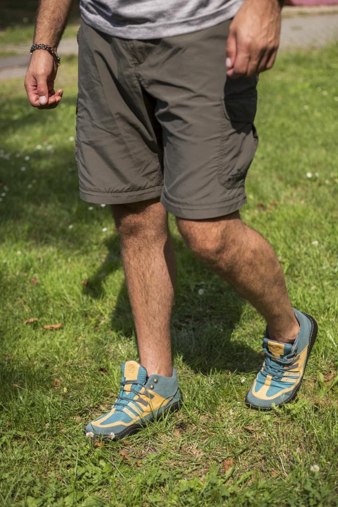 Eine Person läuft auf Gras in grauen Shorts und den robusten ESQAPE Blue Orange Waterproof Sneakers von ZAQQ. Nur ihr Unterkörper ist sichtbar.