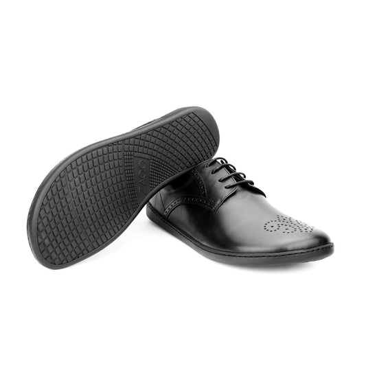 Die schwarzen Abendschuhe PEAQ Brogue Black von ZAQQ aus schwarzem Leder verfügen über ein Schnürdesign mit dezentem Muster auf der Zehenkappe. Ein Schuh ist so ausgestellt, dass die strukturierte Sohle sichtbar ist, was die raffinierte Eleganz der Handwerkskunst von ZAQQ unterstreicht.