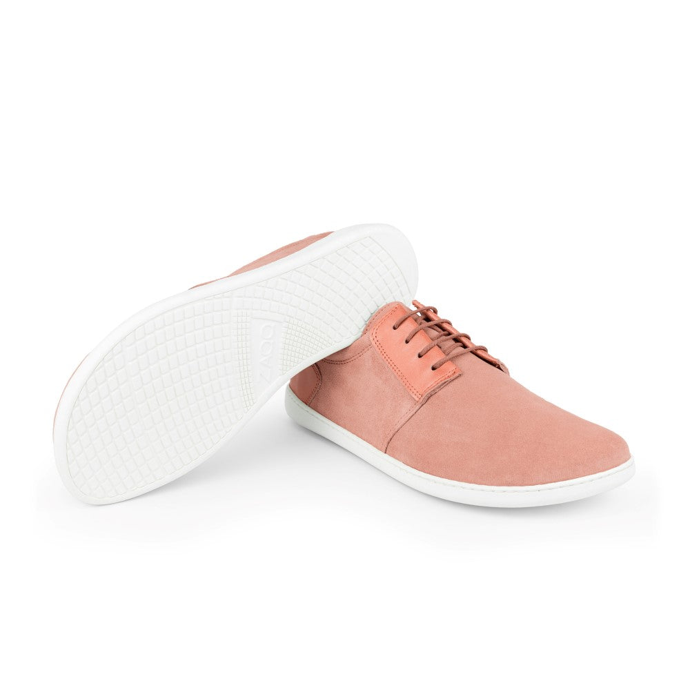 Ein Paar PIQUANT Rosa Sneaker von ZAQQ, gefertigt aus weichem Veloursleder in einem rosa Farbton, mit weißen Sohlen. Ein Schuh steht aufrecht, während der andere auf der Seite liegt und das elegante Design der Sohle zur Geltung bringt.