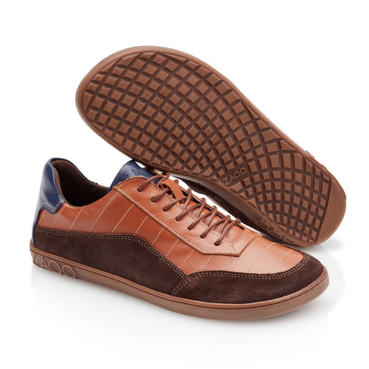 Wir präsentieren den QAMPION Brown von ZAQQ, ein anspruchsvolles Paar Barfuß-Sneaker aus elegantem braunem Leder und dunkelbraunen Wildledereinsätzen. Sie verfügen über stilvolle Schnürungen vorne und auffällige blaue Akzente an den Fersen. Die flexible Kautschuksohle ist mit einem einzigartigen Gittermuster versehen und der Markenname ZAQQ ist sowohl auf der Sohle als auch an der Seite deutlich sichtbar, was ihr raffiniertes Erscheinungsbild unterstreicht.