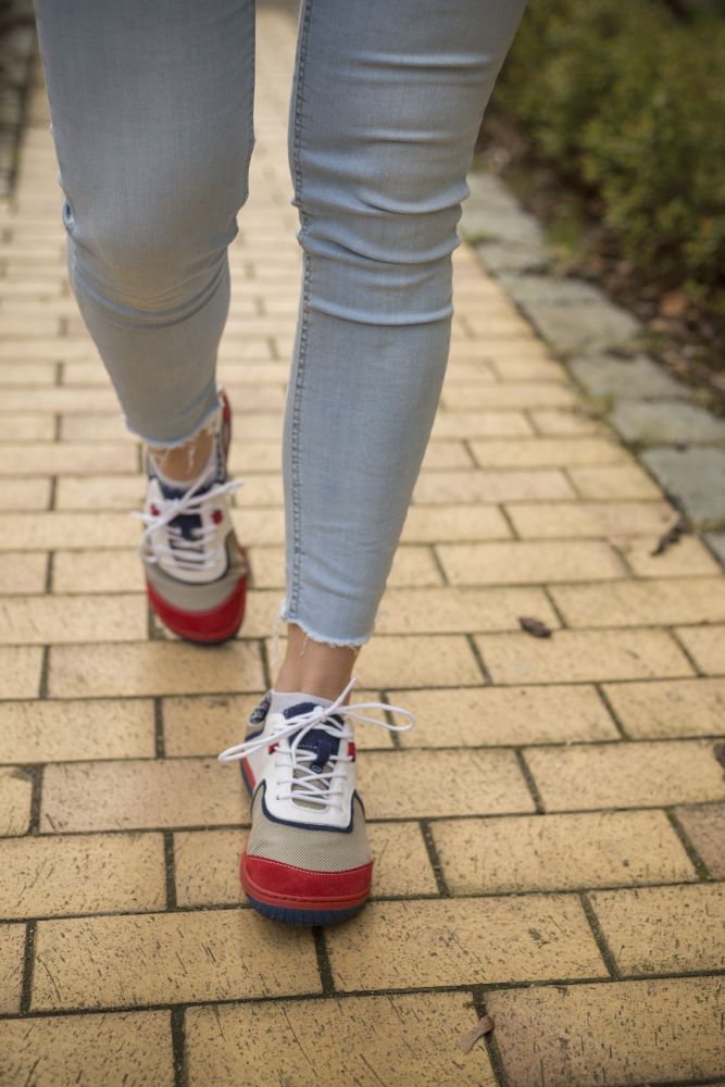 Eine Person in hellblauen Jeans und den stylischen weißen QOLETTE-Sneakern von ZAQQ geht gemütlich auf einem gelben Backsteinweg und stellt dabei mühelosen Stil zur Schau.