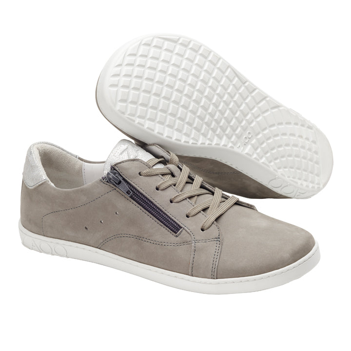 Wir präsentieren die QOMFY Wide Grey Sneaker von ZAQQ: Diese schicken grauen Sneaker zeichnen sich durch ein raffiniertes Obermaterial aus Veloursleder aus, ergänzt durch weiße Sohlen und beige Schnürsenkel. Ein Schuh steht aufrecht und hebt den praktischen seitlichen Reißverschluss hervor, während der andere geneigt ist und seine gitterförmige strukturierte Sohle zeigt, die für mehr Komfort sorgt.