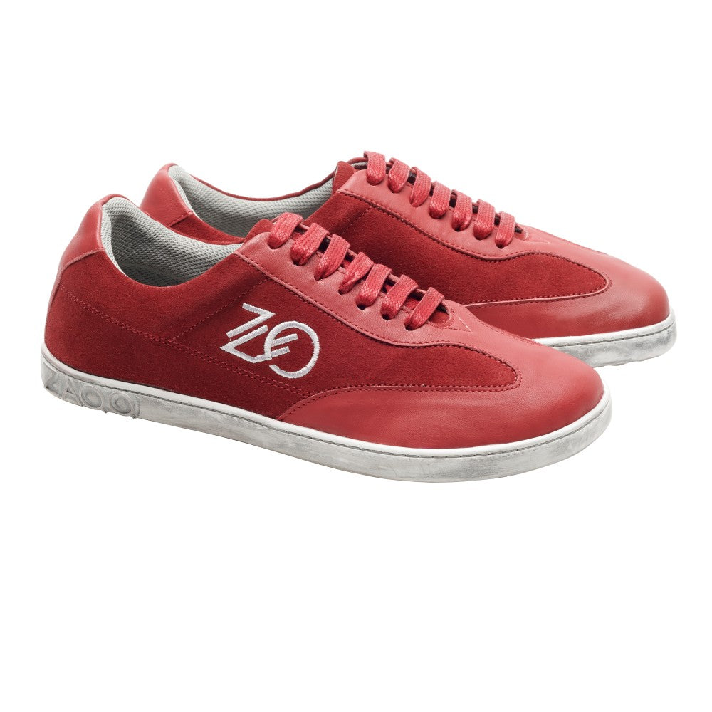 Wir präsentieren den Queensburry Robin von ZAQQ: ein Paar roter Barfuß-Sneaker mit weißer Sohle und Schnürsenkeln, verziert mit einem stylischen Logo an den Seiten. Dieses Design kombiniert kunstvoll rotes Leder und Wildleder für ein elegantes Erscheinungsbild vor einem schlichten weißen Hintergrund.