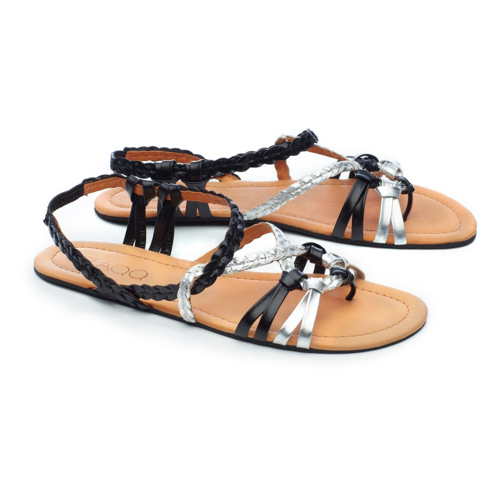 Die FRESQO Black Silver Sandalen von ZAQQ sind ein Paar flache Sandalen mit geflochtenen schwarzen Riemen und metallisch-silbernen Akzenten, einem offenen Zehendesign und einem hellbraunen Fußbett, perfekt für Liebhaber von Barfußsandalen, die schicke Sommeroutfits ergänzen möchten.