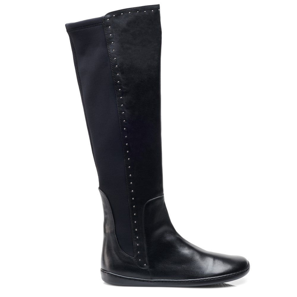 Ein hoher schwarzer Lederstiefel namens QATCH SHINE Nappa Black von ZAQQ mit dekorativen Nieten an den Seiten. Der Stiefel zeichnet sich durch ein schlankes Design, eine glatte Textur und eine flache Kautschuksohle aus, wodurch er sowohl für Freizeit- als auch für formelle Anlässe geeignet ist.