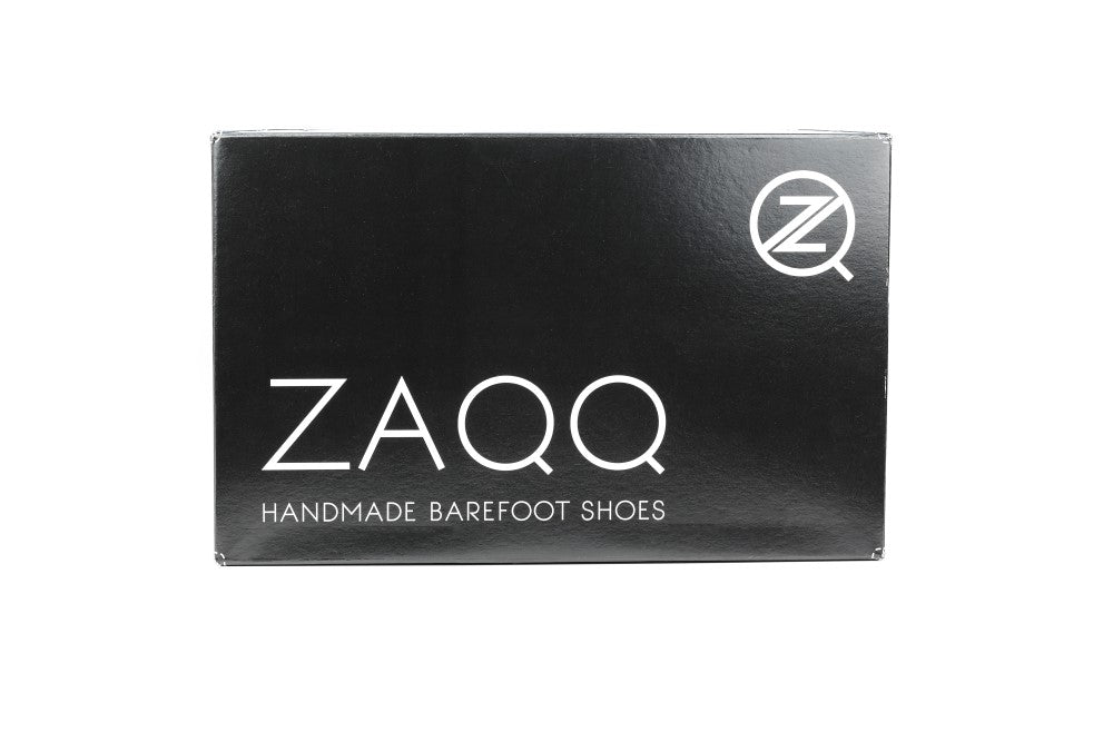 Eine elegante rechteckige schwarze Box zeigt prominent das ZAQQ-Logo neben dem Slogan „Handmade Barefoot Shoes“ in Weiß. In der oberen rechten Ecke befindet sich ein stilisiertes Z-Emblem. Diese anspruchsvolle Verpackung hebt den ZAQQ QISS Black-Schuh, der fachmännisch aus hochwertigem Nappaleder gefertigt wurde, vor einem schlichten weißen Hintergrund hervor.