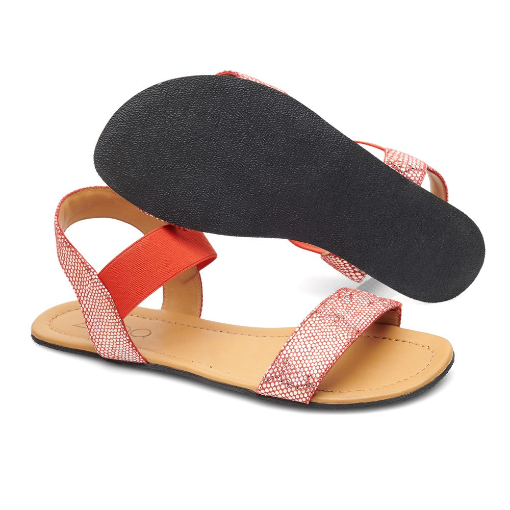 Ein Paar ZAQQ SLIQ-Red Sandalen mit orangefarbenen Stoffriemen und einem dezenten geometrischen Muster. Die Sohlen sind schwarz, wobei die Sohle einer Sandale nach oben zeigt, um die strukturierte Oberfläche zu zeigen. Das Fußbett ist hellbraun und sorgt für ultimativen Komfort und ein natürliches Tragegefühl.