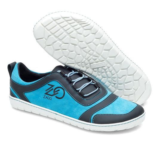 Wir präsentieren die SQILL Turquoise Black Sneaker von ZAQQ, die sich durch ein auffälliges türkis-schwarzes Farbschema mit weißen Sohlen auszeichnen. Ein Schuh steht aufrecht und zeigt deutlich das ZAQQ-Logo auf der Seite, während der andere seine strukturierte Sohle zur Schau stellt. Das Design ist für außergewöhnlichen Tragekomfort bekannt und wird durch blaue Schnürsenkel sowie kontrastierende dunkle und helle Details aufgewertet.