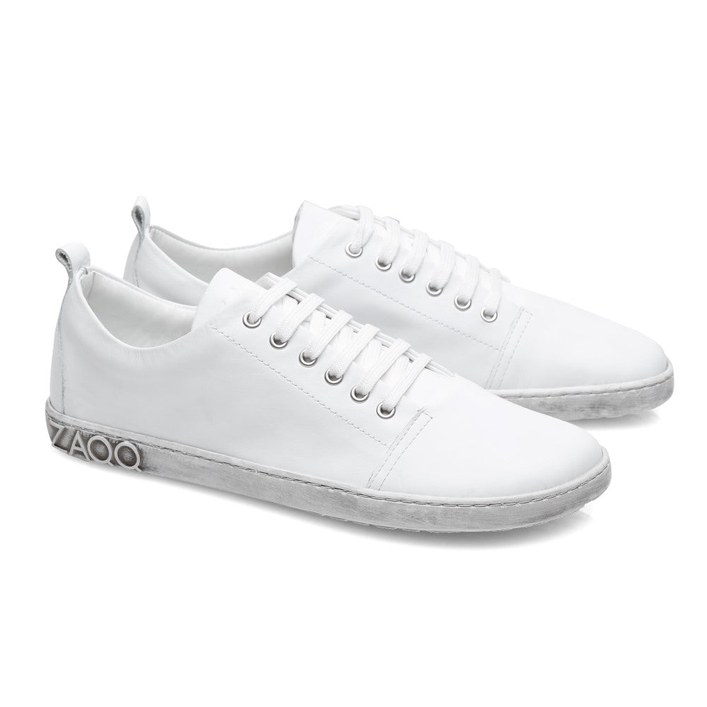 Die TAQQ Nappa White Sneaker von ZAQQ sind aus hochwertigem Nappaleder mit weißen Schnürsenkeln und hellgrauen Kautschuksohlen gefertigt. Sie zeichnen sich durch ein minimalistisches Design, eine kleine Fersenschlaufe und ein markantes Logo auf der Zwischensohle des linken Schuhs aus.