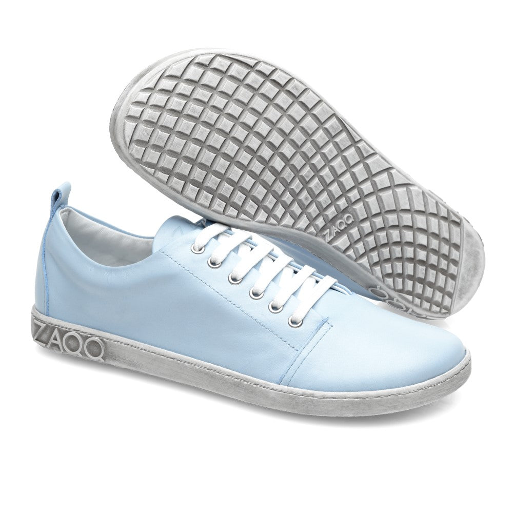 Ein Paar TAQQ Nappa Lightblue-Sneaker von ZAQQ mit weißen Schnürsenkeln und Sohlen. Ein Schuh ist aufrecht abgebildet und zeigt sein Seitenprofil, während der andere geneigt ist und die strukturierte, flexible Sohle zeigt. Der Markenname ZAQQ ist sowohl an der Seite als auch an der Sohle deutlich sichtbar und sorgt für ein elegantes Finish.