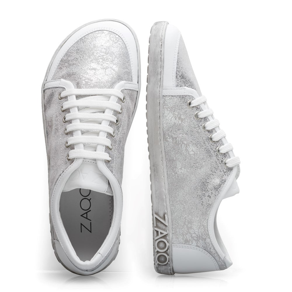 Wir präsentieren die TIQQ Silver White Sneaker von ZAQQ in schickem Design aus Premium-Nappaleder mit einzigartiger marmorartiger Textur und weißen Schnürsenkeln. Der Markenname ist prominent auf der Sohle eines Sneakers angebracht. Diese Barfußschuhe sind elegant nebeneinander vor einem weißen Hintergrund positioniert.